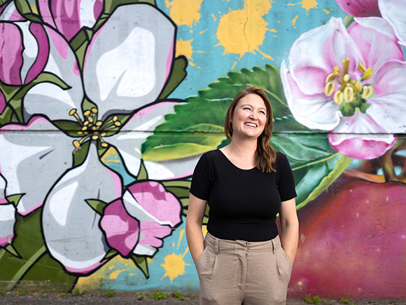 A graduate of the Nonprofit Leadership program stands in front of a floral mural and smiles.