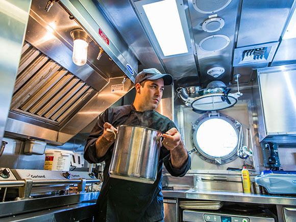 A man carries a pot in a ship's galley.