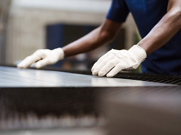 Arms and gloved hands are pictured over a piece of sheet metal.