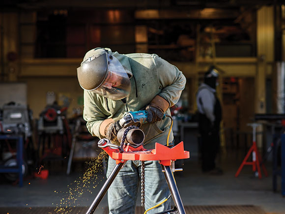 A man in protective wear works on a piece of metal pipe.