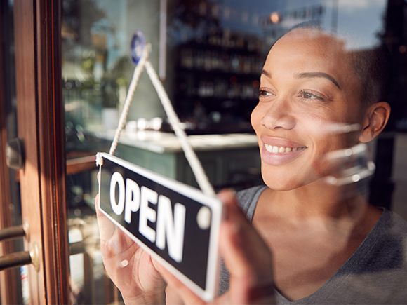 An African Canadian woman smiles as she posts an open sign on the door of her new business.