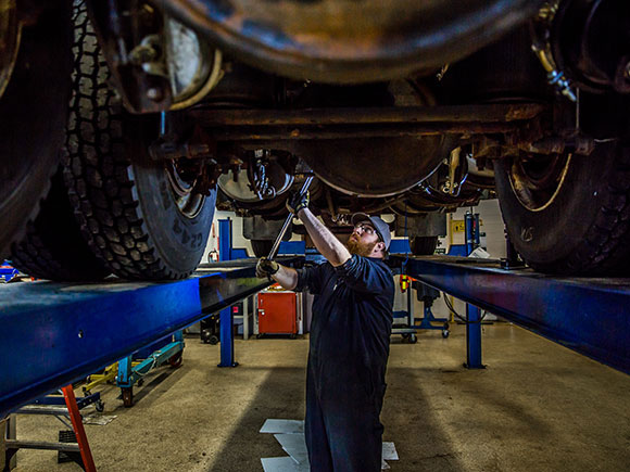 A mechanic works under a hoisted vehicle.