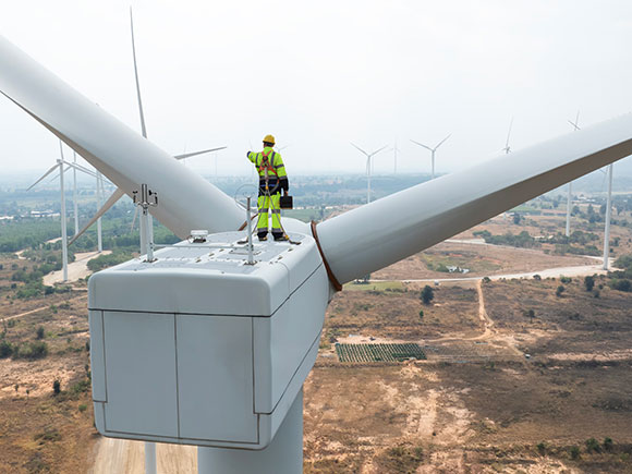 A wind turbine technician stands on top of a wind turbine overlooking a wind farm.