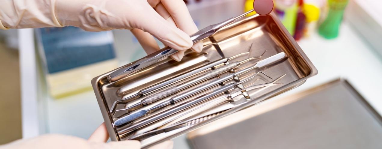 Gloved hands selecting a dental instrument from a sterilized tray in a clinical setting.