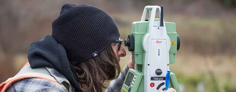 Two people wearing safety vests and using surveying equipment in an outdoor setting.