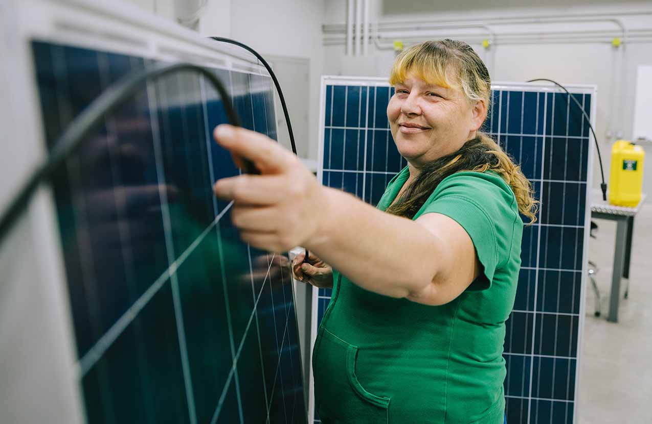 A women in a green sweater is standing among two solar panel adjusting the wires.