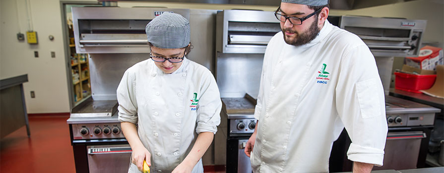 A female apprentice in the kitchen with her mentor. 