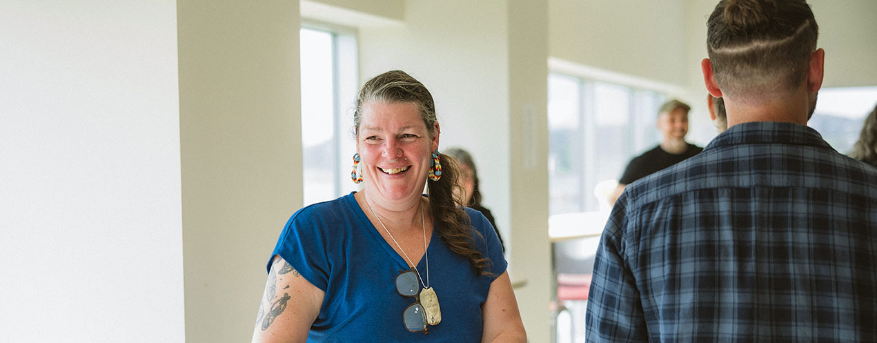 A small group of students stand in a classroom with large windows. One smiling student is in the foreground.