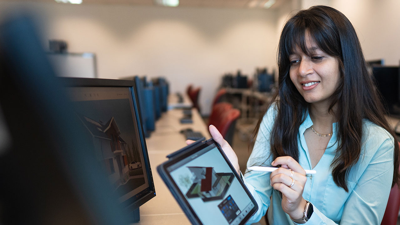 A female student looks at a rendering on her tablet and computer screen.
