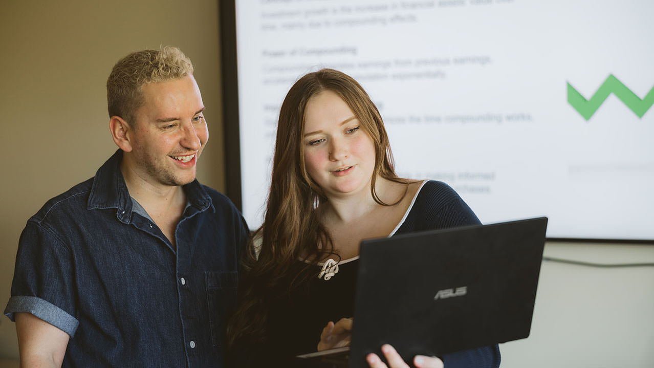 Two NSCC Business Administration students stand and look at an open laptop together.