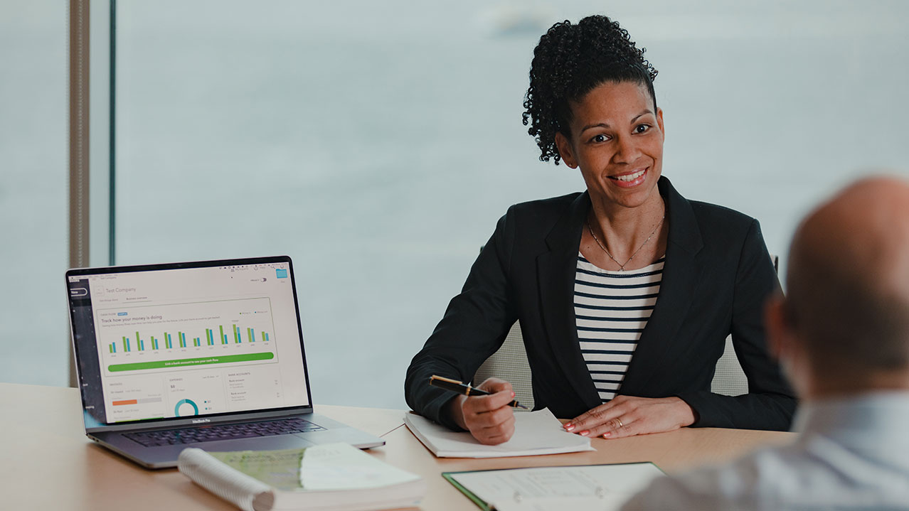 A professionally dressed woman sits at a conference table.