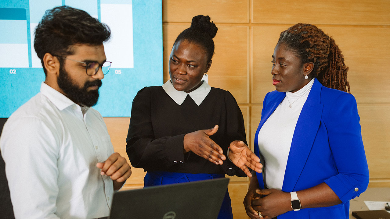 A Business Analysis grad talks to other students in the program while looking at a laptop together.