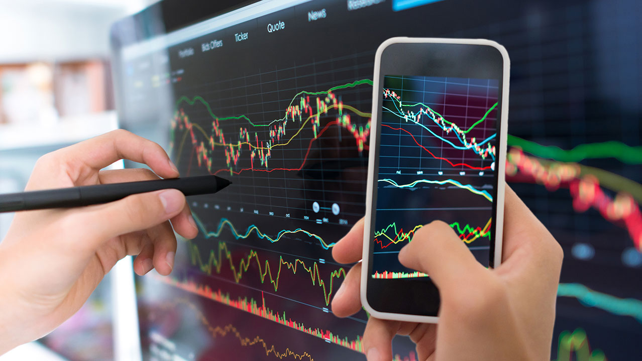A close-up photo of a hand drawing graphs and charts on a tablet screen and another hand holding a smartphone.