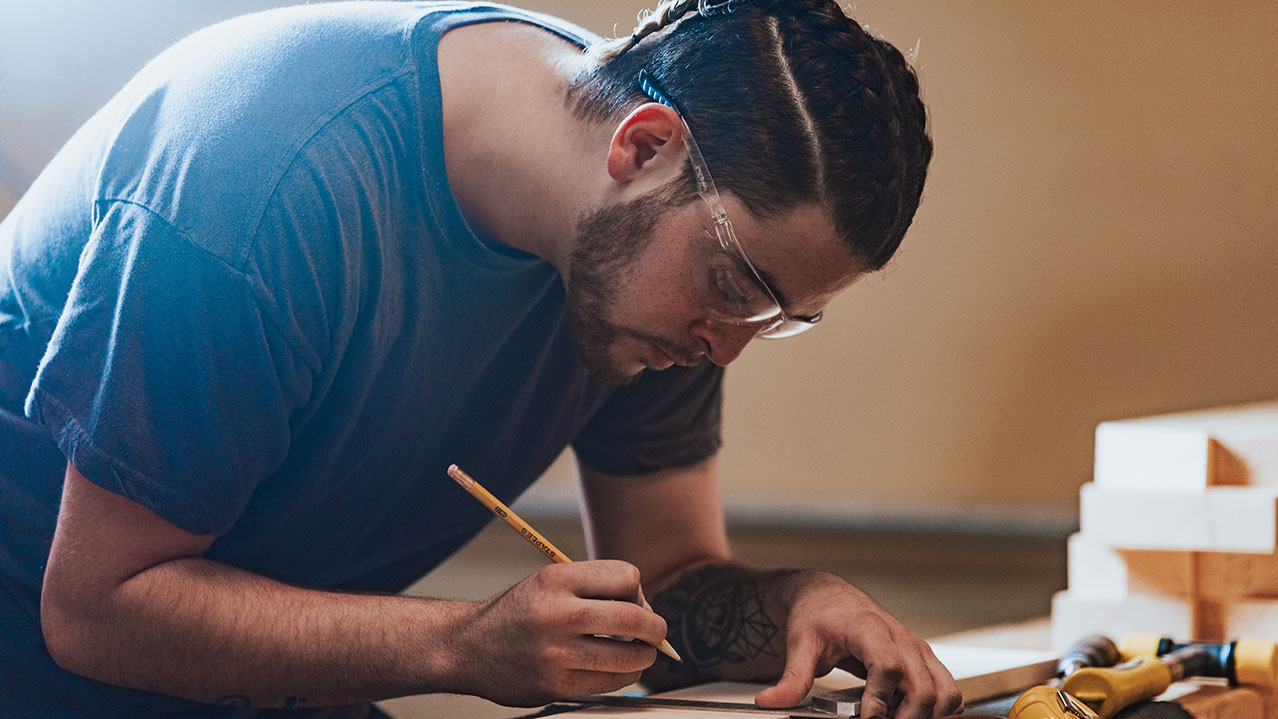 A student measures lumber on a shop table at NSCC.