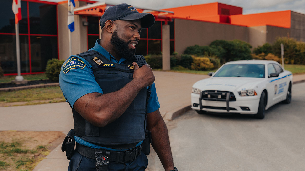 A man in a sheriff's uniform talks into a shoulder walkie talkie while standing in front of a stone building.