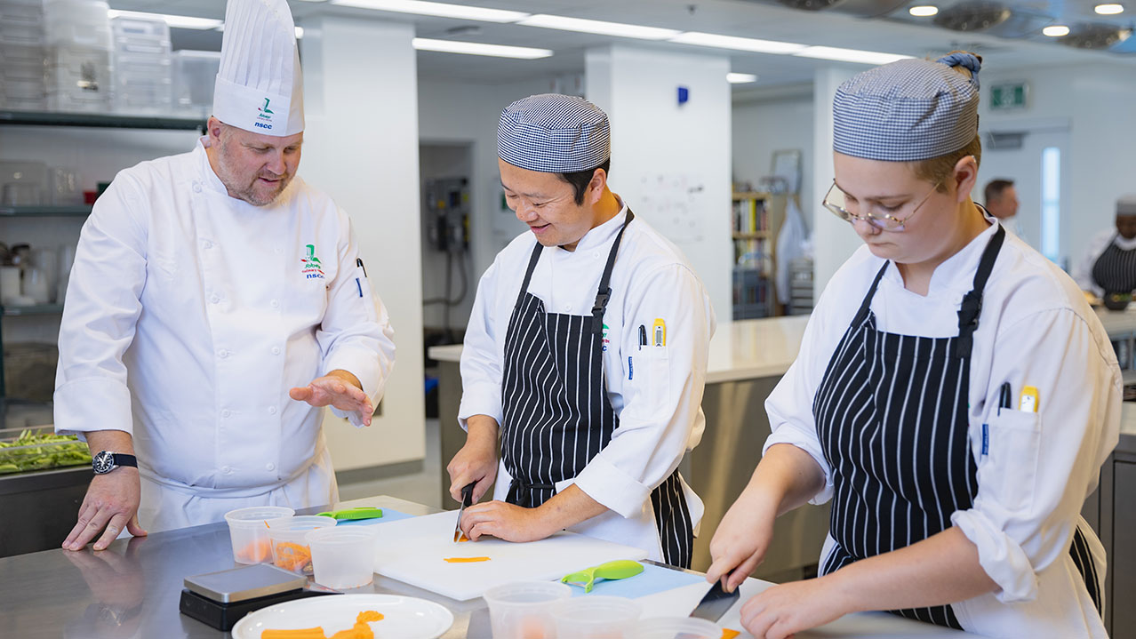 An instructor teaches 2 students knife skills at NSCC.