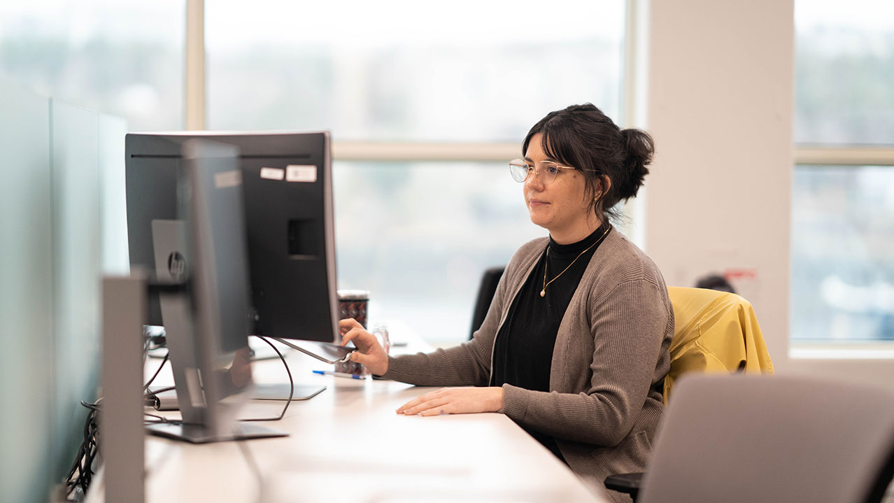 A woman in glasses sits working at her computer.