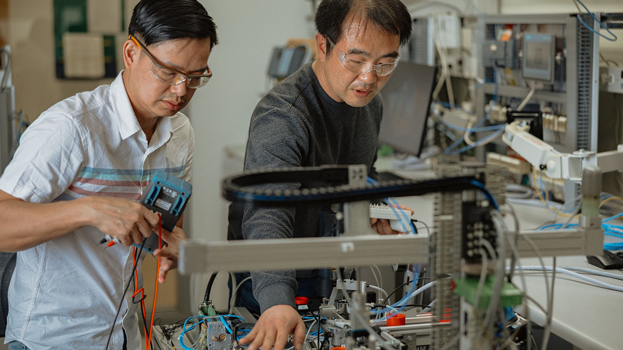 A student works on a machine with lots of wires while the faculty explains about the machine. 