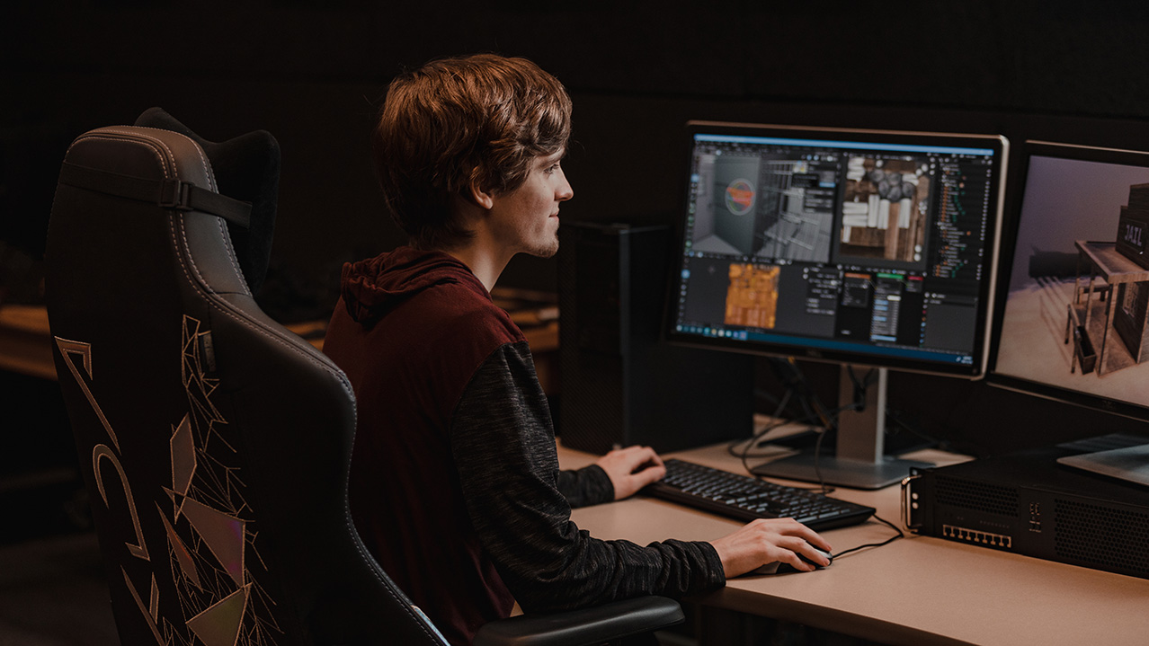 A student sits in front of multiple monitors.
