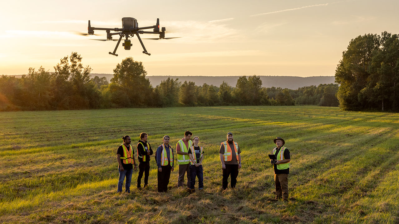 A group of COGS students and an instructor fly a drone in an open field.