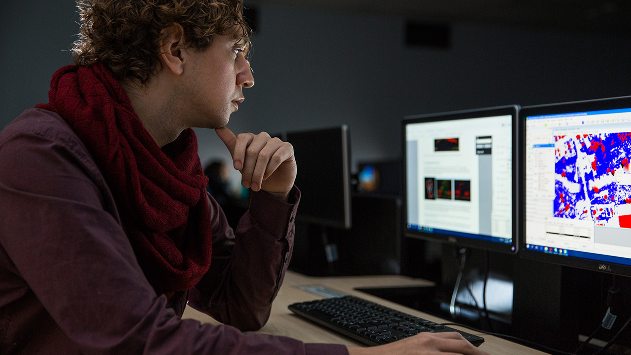 A man sits in front of multiple monitors displaying geographic information data.
