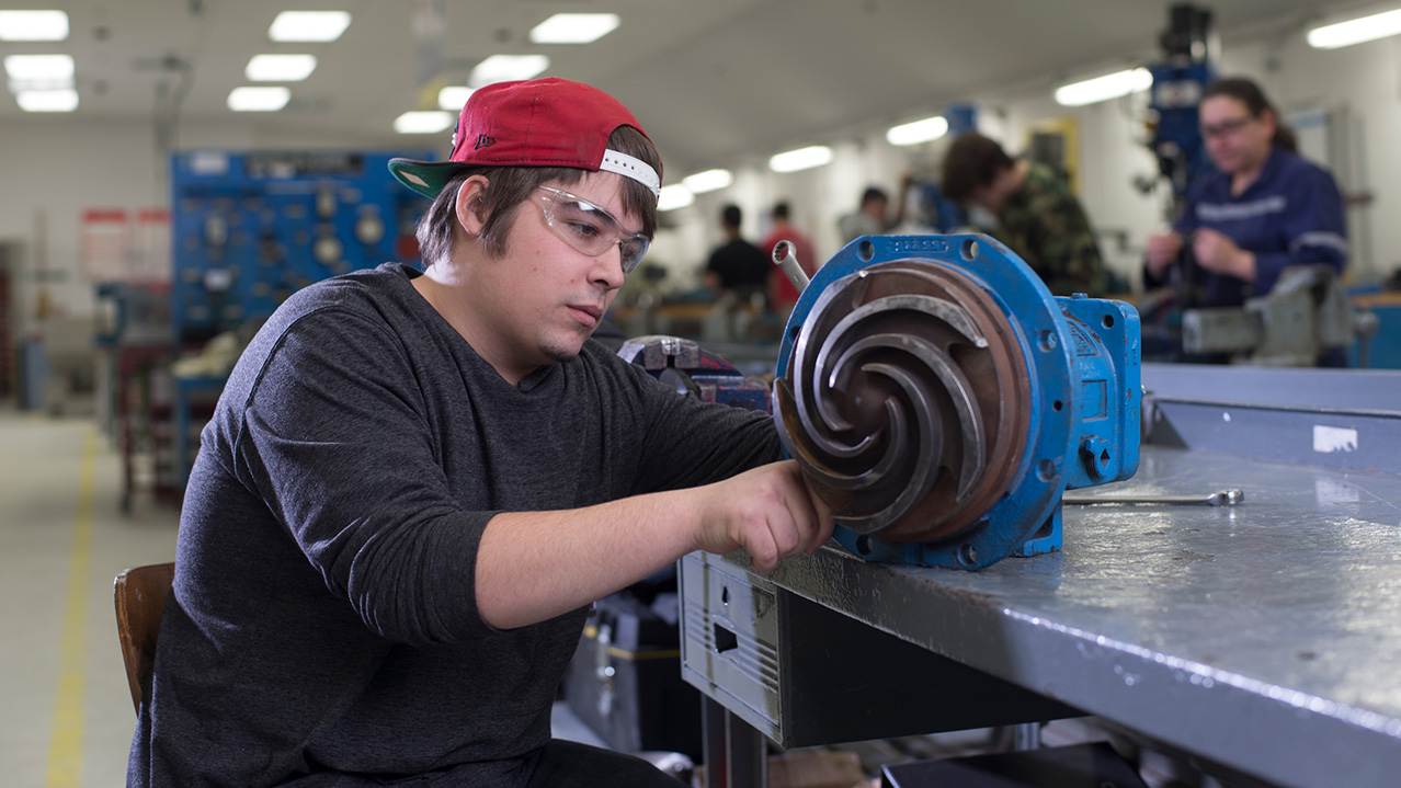A man in protective eye goggles works on a small piece of mechanical equipment.