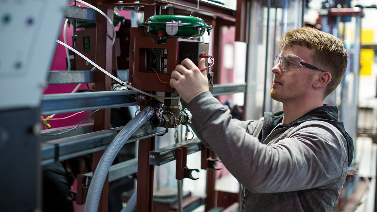 A man in protective eye goggles works on a piece of equipment for his instrument technician diploma course.
