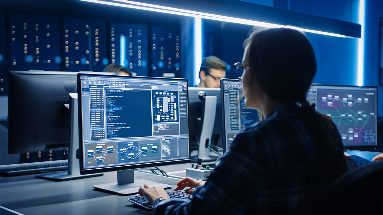 An office setting with several people sitting in front of computers and programming.