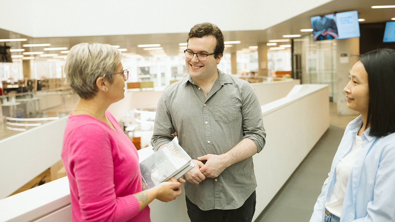 Three students from the Library and Information Technology program are seen talking in a large library setting.
