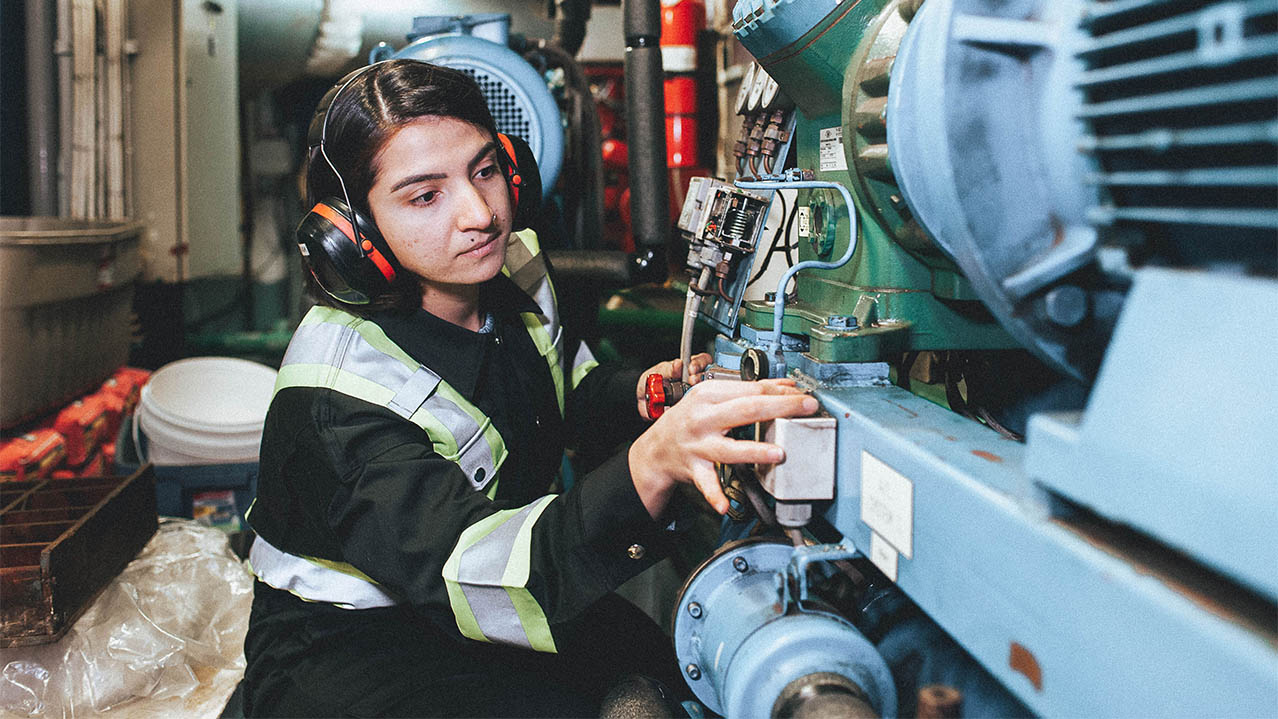 An NSCC Marine Engineering Technology student in protective gear works on engine room equipment.