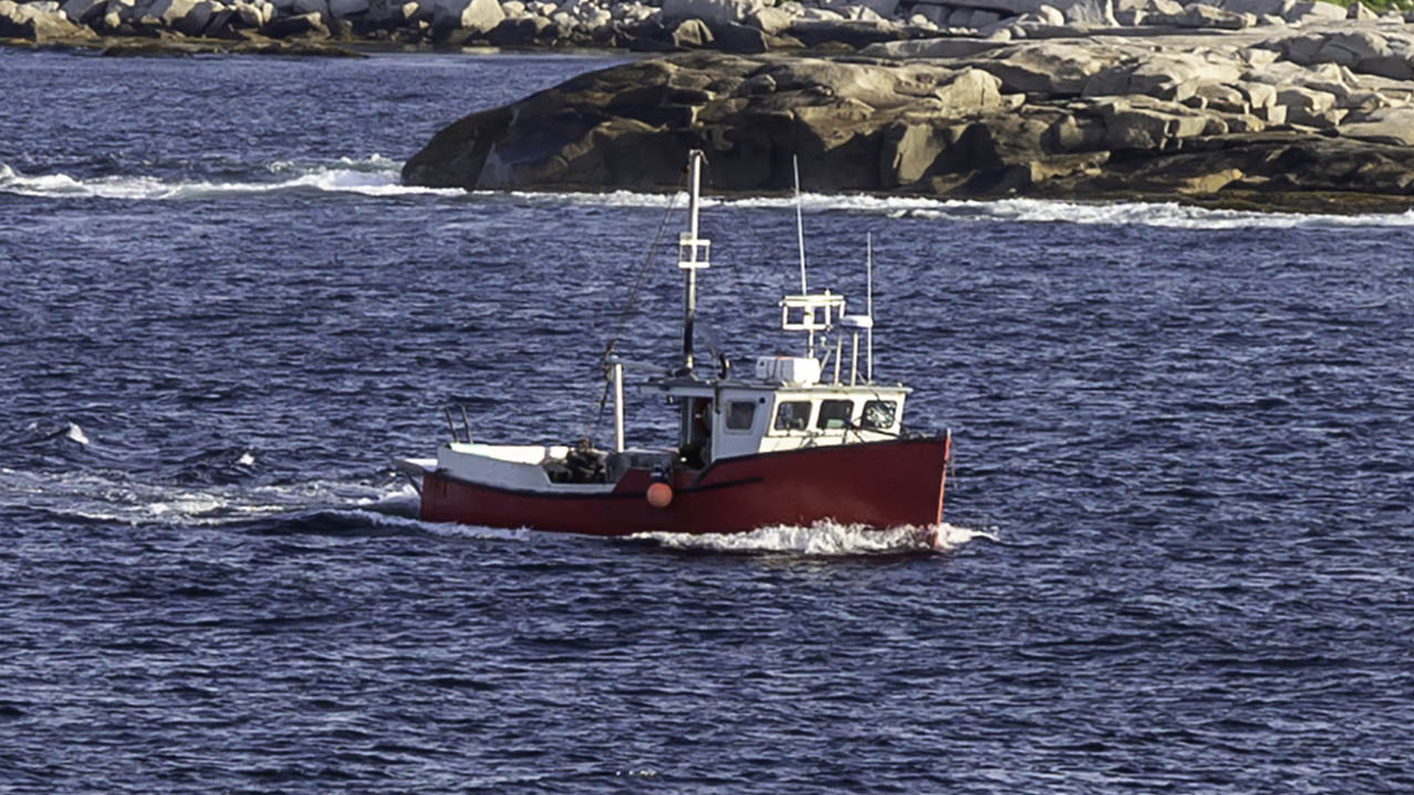 A small red fishing boat sails along the coastline.