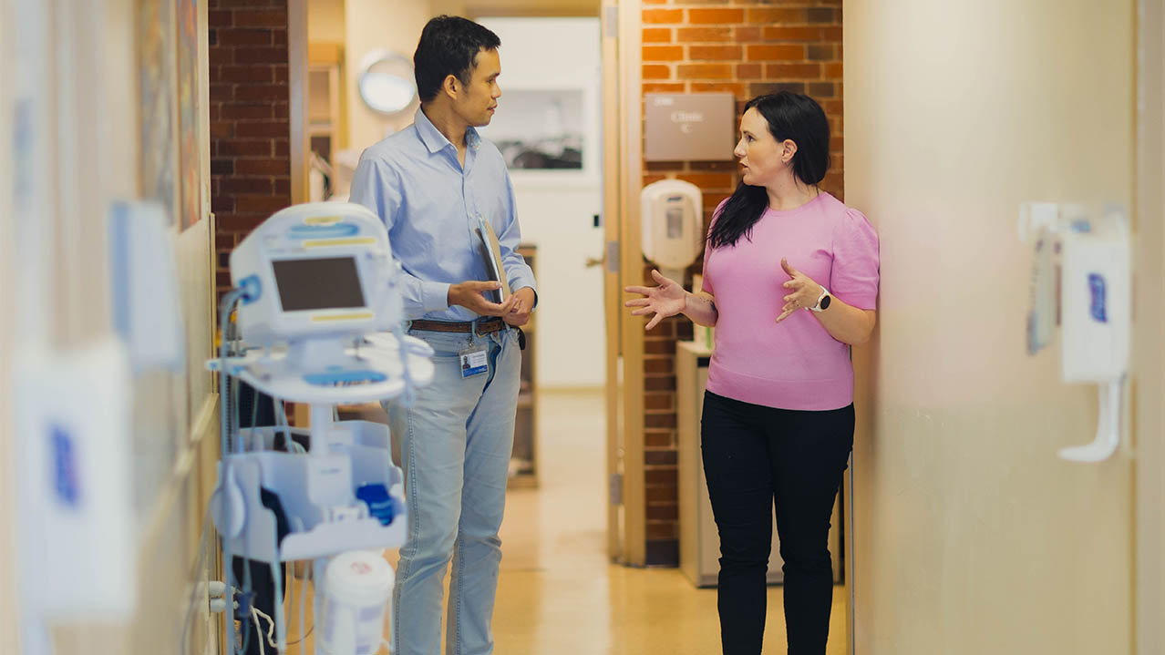 Two Medical Office Administration graduates walking down a hallway and talking in a hospital setting.