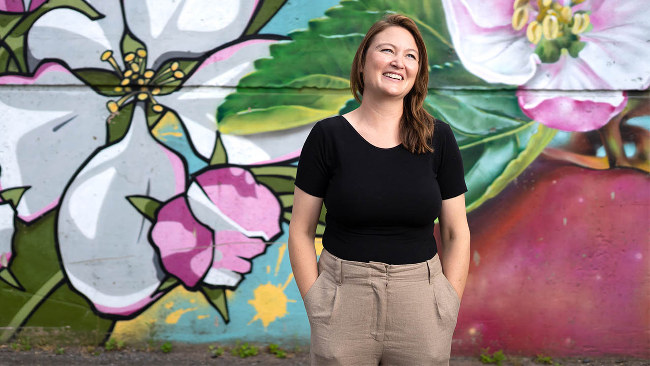 A graduate of the Nonprofit Leadership program stands in front of a floral mural and smiles.
