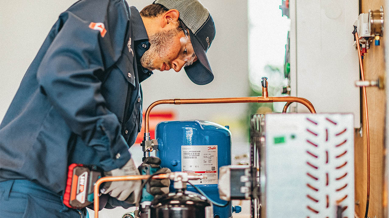 A man, holding a tool in his hand, works on a mechanical system.