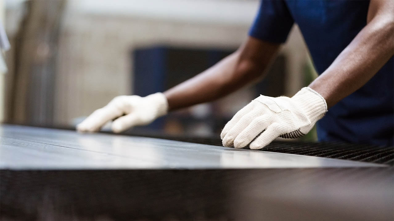 Arms and gloved hands are pictured over a piece of sheet metal.
