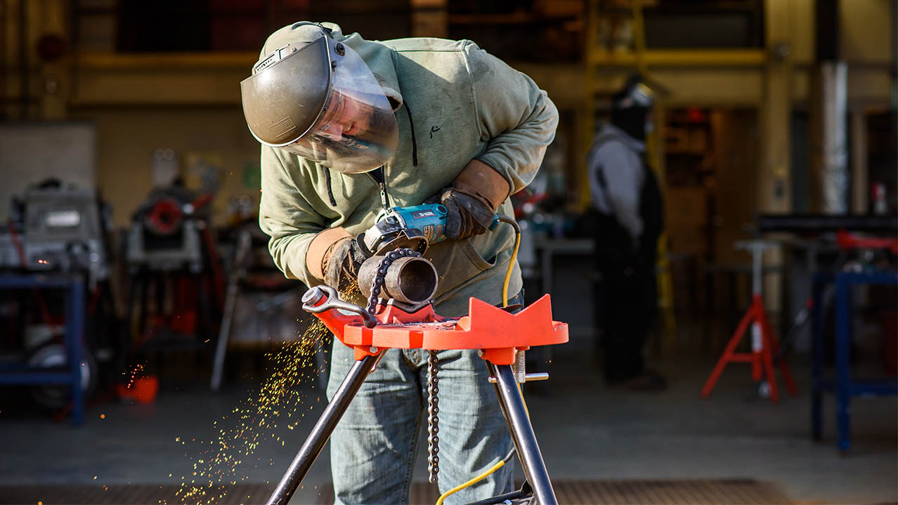 A man in protective wear works on a piece of metal pipe.
