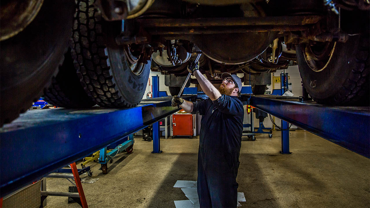 A mechanic works under a hoisted vehicle.