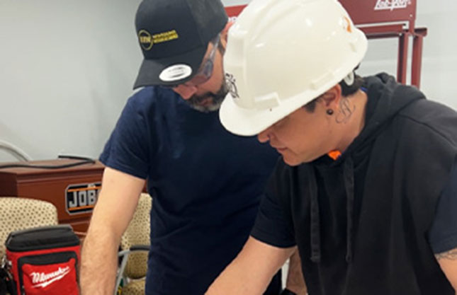 A student is seen smiling at the camera in a lab setting wearing a hard hat for his Plumbing program.