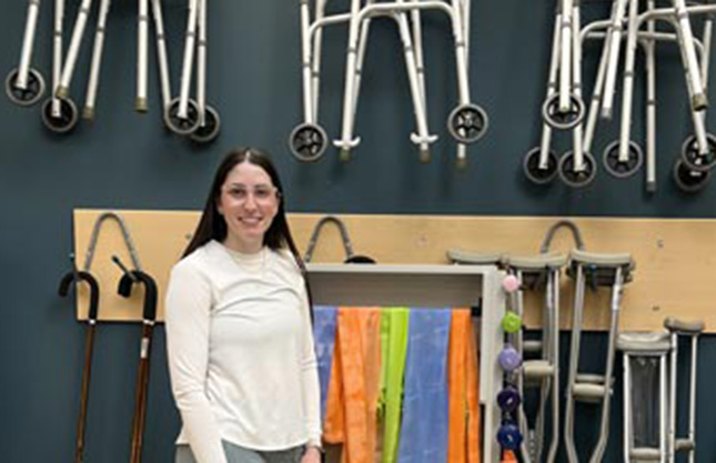 NSCC student Jessie stands by a wall of mobility devices such as canes and walkers at Amherst Learning Centre, part of Cumberland Campus.