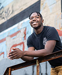 Keandre looks skyward as he leans on the railing of a concrete balcony.