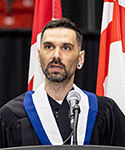Shaun stands behind a podium wearing his graduation gown and hood.