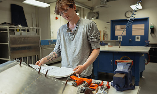 An aircraft maintenance diploma student reads a manual and prepares to work on an aircraft component.