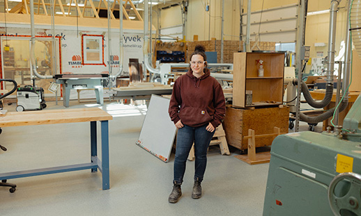 A student in NSCC carpentry courses stands in a carpentry workshop and looks at the camera.