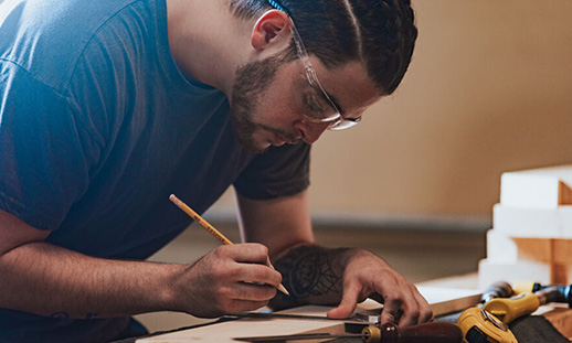 A Nova Scotia carpentry programs student uses a pencil and ruler to mark a measurement on a piece of wood.