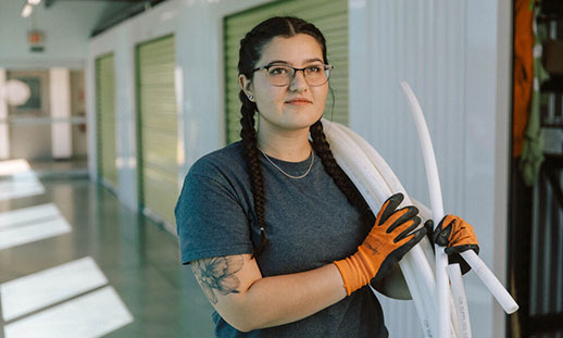 Taylor, an NSCC Plumbing grad, Carries a roll of plastic pipe while walking down a hallway.