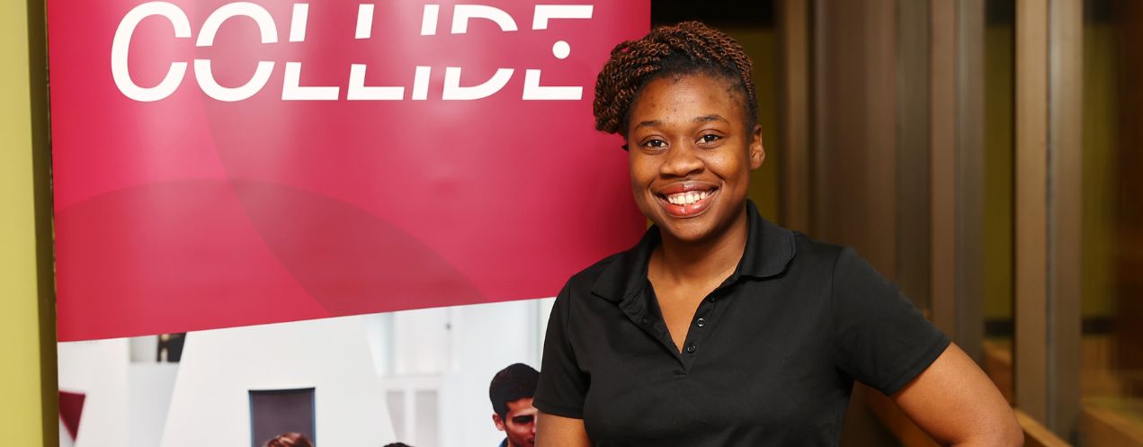 Woman in a black shirt smiling and standing in front of a Collide program banner.