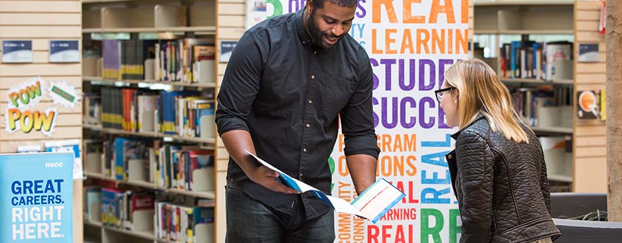 Man standing and helping a woman in the library. 