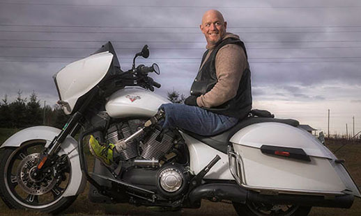 Eric Payne sits on a motorbike and smiles at the camera.