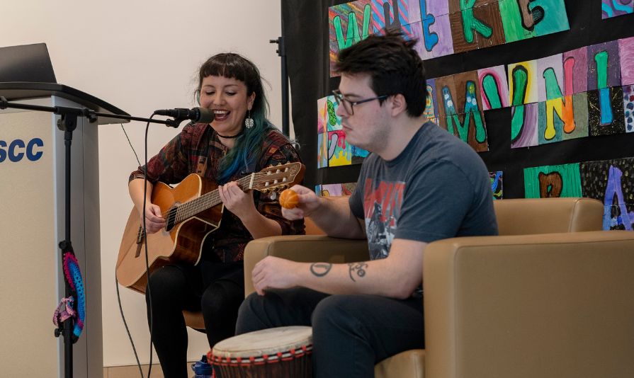 Two students playing guitar and a hand drum during an event.