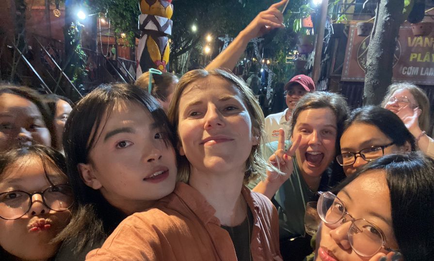 Group selfie of smiling students at night in a lively outdoor area.